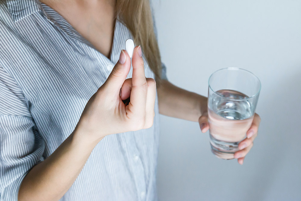 Witamina D3: kobieta trzyma tabletkę i wodę w rękach
