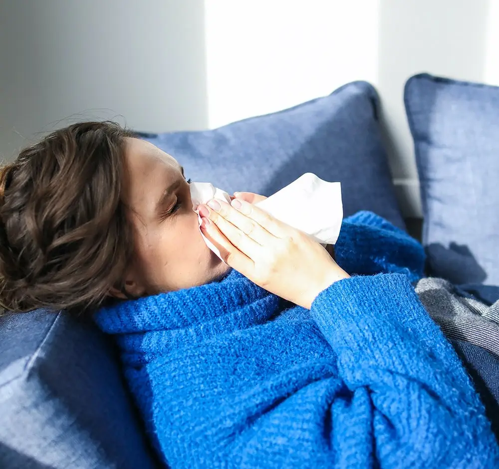 Flu: a woman is sick in bed, sneezing into a white napkin