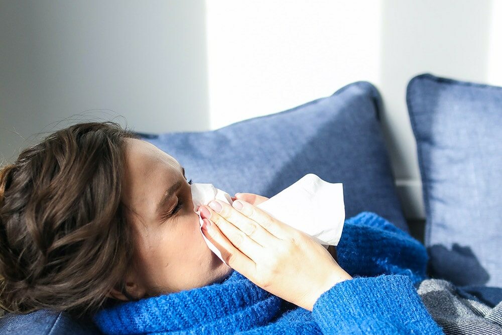 Grypa: kobieta leży w łóżku chora, kicha do białej serwetki