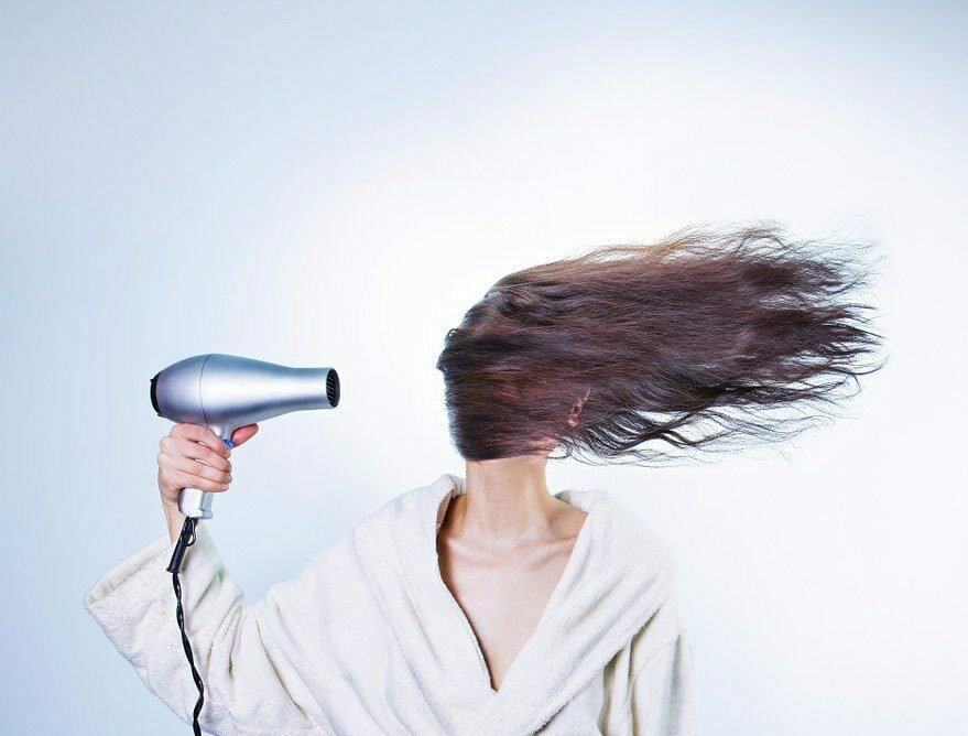 Kobieta suszy długi ciemne włosy suszarką, obrazek do artykułu na temat łysienia