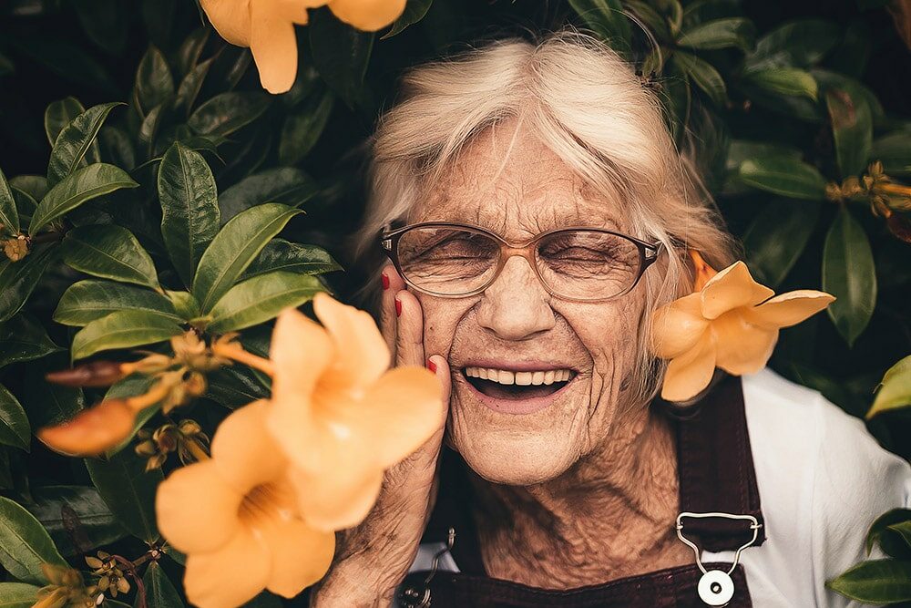 Menopause: a beautiful older lady smiles, against the background are yellow flowers.