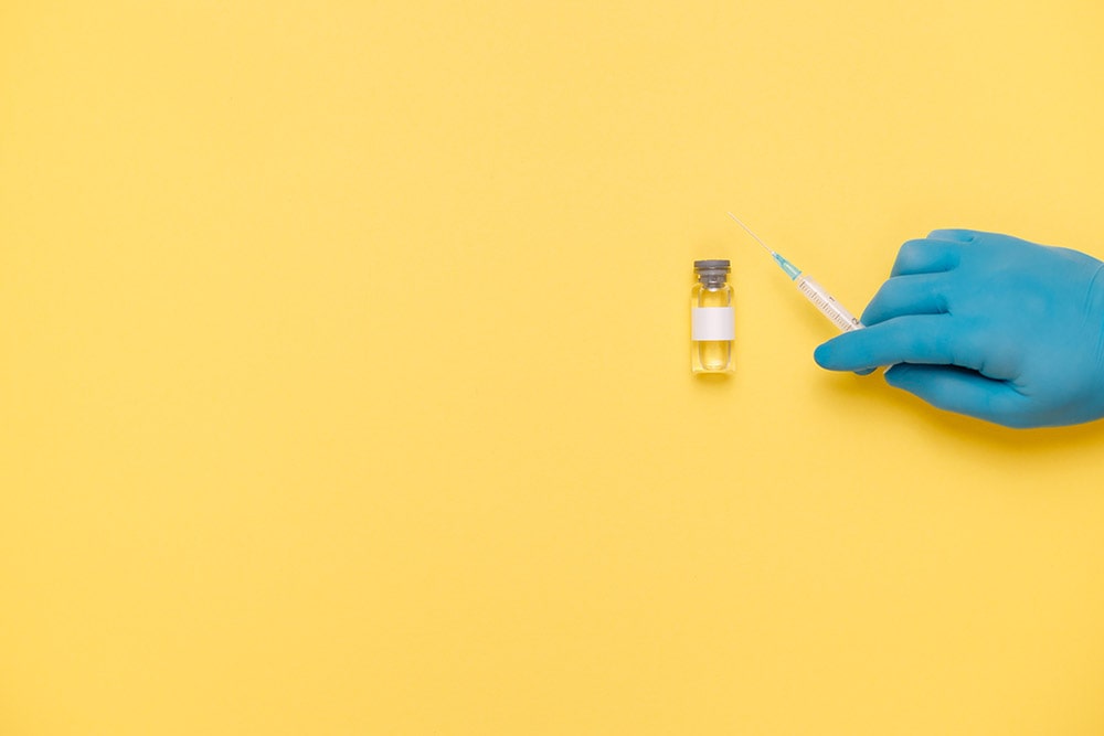 Insulin is lying on the yellow table, a hand in a blue medical glove is holding a syringe