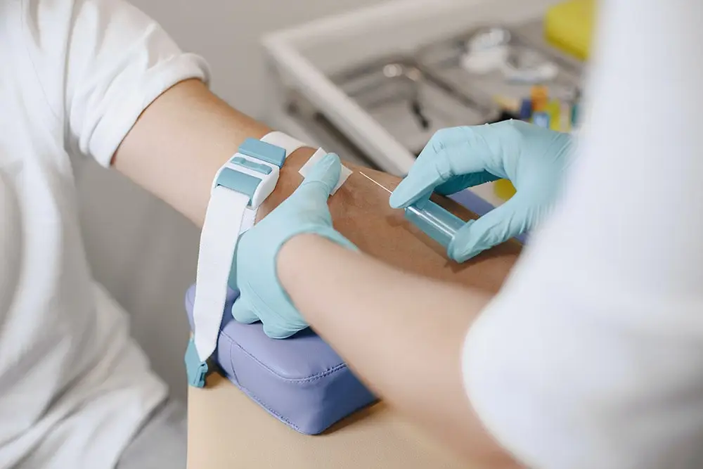 a doctor in blue gloves draws blood from a patient wearing a white shirt to do a control tests