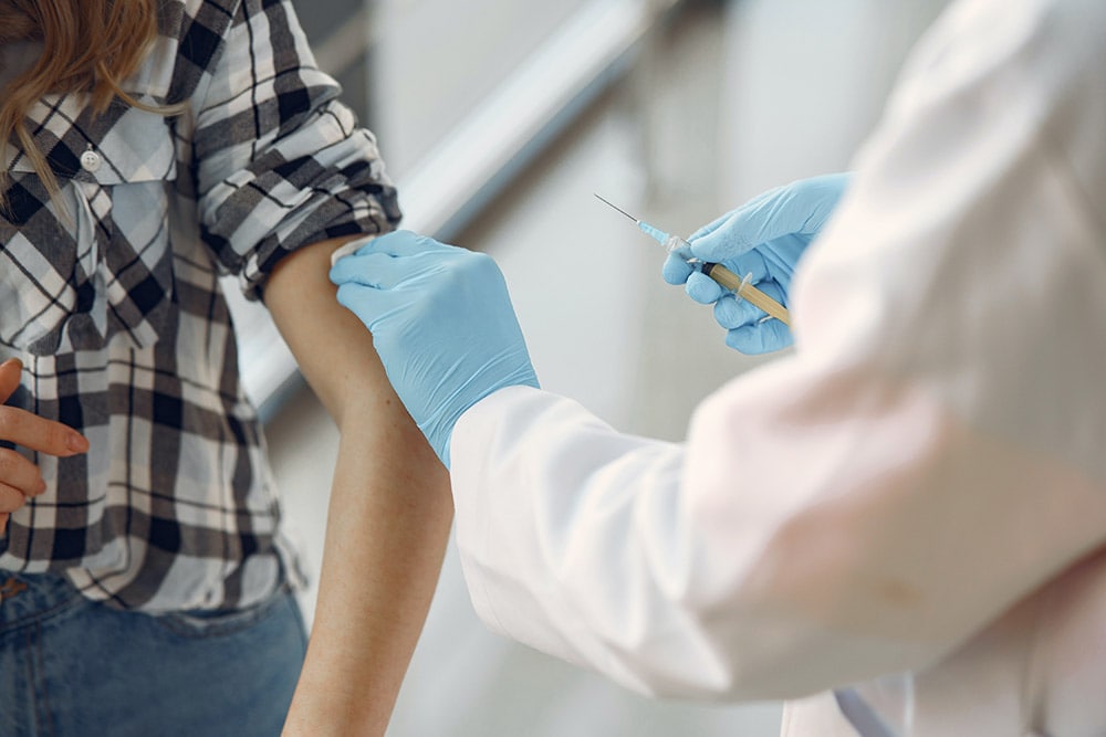 Szczepionka: Lekarz ubrany w biały fartuszek i niebieskie rękawiczki robi szczepienie dla Pani w koszule