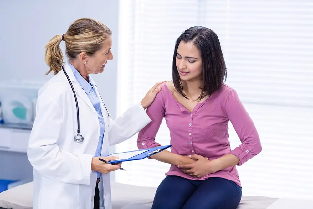 A lady in a pink T-shirt is sitting in the doctor's office complaining of IBD