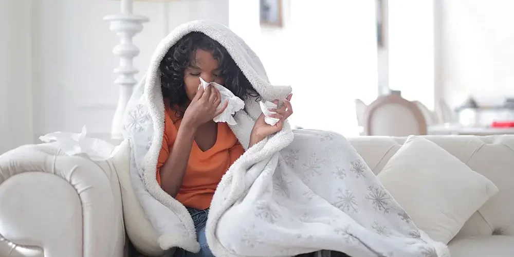 A girl sitting on the couch wrapped in a blanket has symptoms of West Nile virus