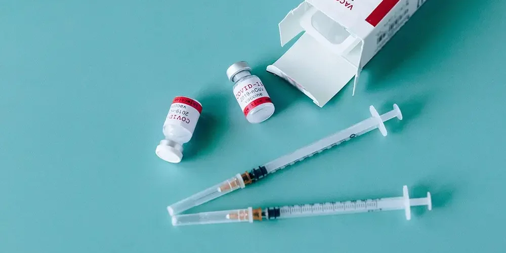 COVID-19 vaccine: there are two syringes, two vaccines and a COVID-19 vaccine box on a blue background