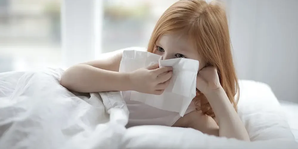 Allergic diseases: A girl with red hair is lying on the bed holding a napkin in her hand in front of her face, she has allergic rhinitis.