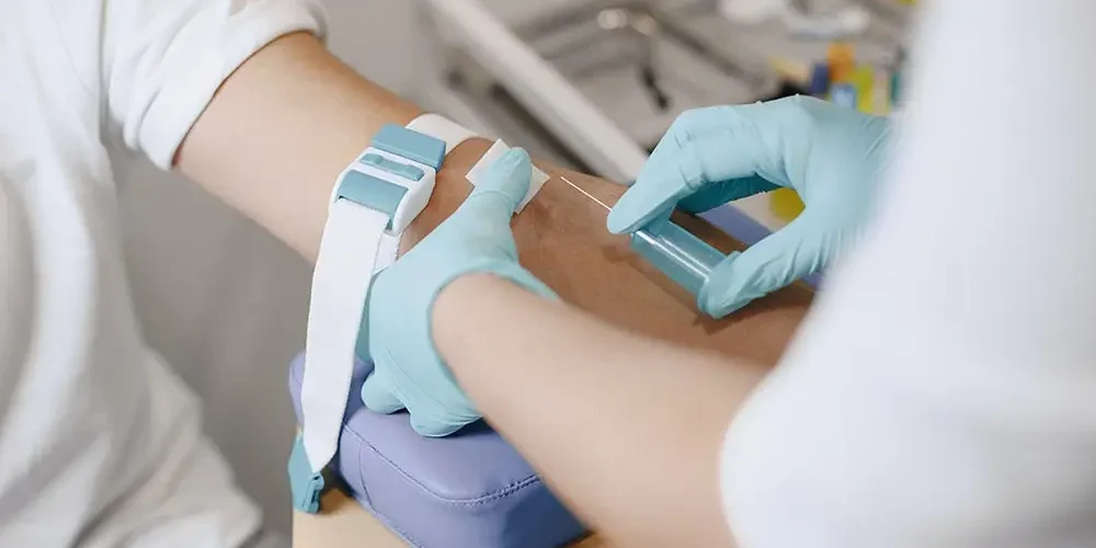 a doctor in blue gloves draws blood from a patient wearing a white shirt to do a control tests