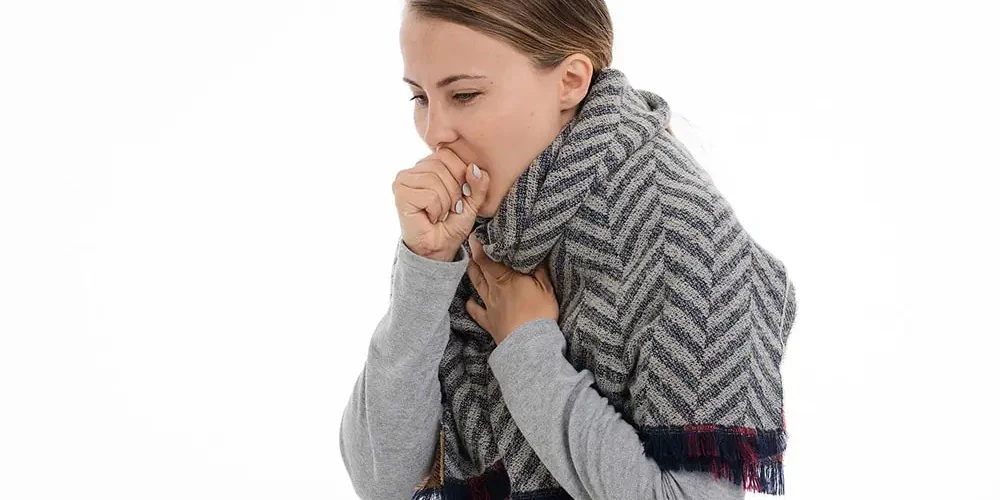 Kobieta ubrana w szary sweter i szalik kaszla