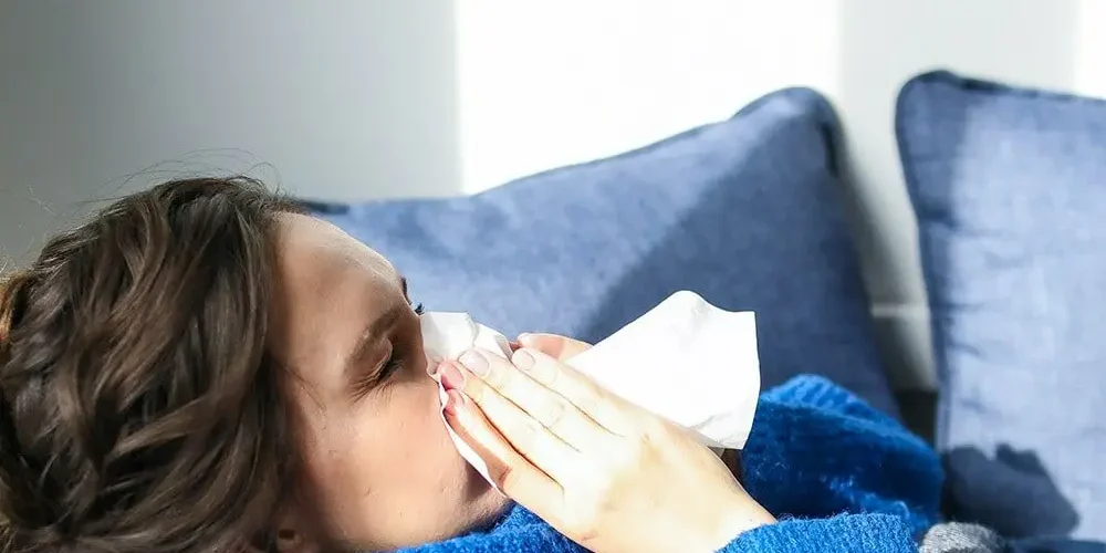 Grypa: kobieta leży w łóżku chora, kicha do białej serwetki