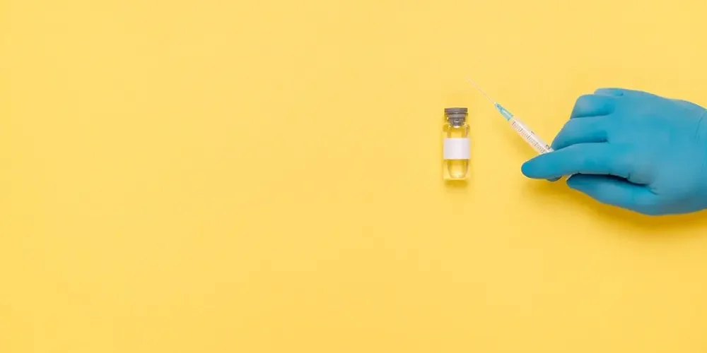 Insulin is lying on the yellow table, a hand in a blue medical glove is holding a syringe