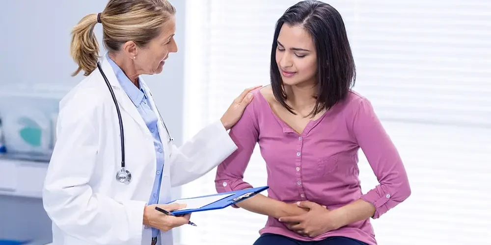 A lady in a pink T-shirt is sitting in the doctor's office complaining of IBD