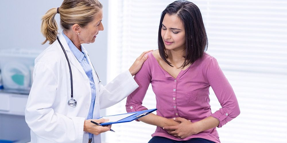 Pani w różowej koszulce siedzi w gabinecie u lekarza i skarży się na Nieswoiste zapalenia jelit