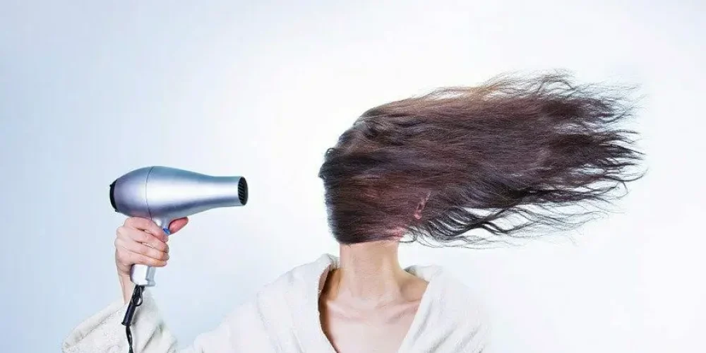 Kobieta suszy długi ciemne włosy suszarką, obrazek do artykułu na temat łysienia