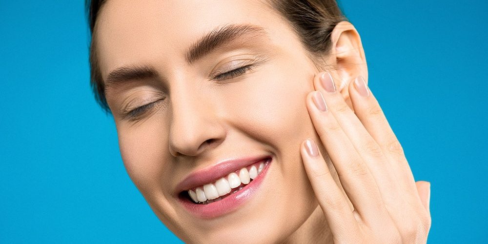 Głowa ładnej Pani na niebieskim tle dotyka Swoją twarz po zabiegu kosmetycznym