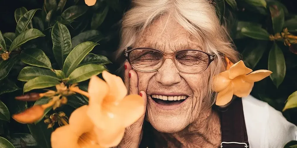 Menopause: a beautiful older lady smiles, against the background are yellow flowers.