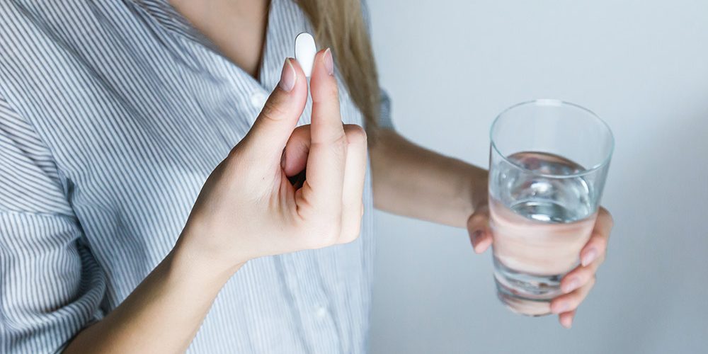 Witamina D3: kobieta trzyma tabletkę i wodę w rękach