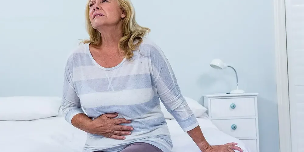 The lady is sitting on the bed, has symptoms of food poisoning, has her hand on her stomach